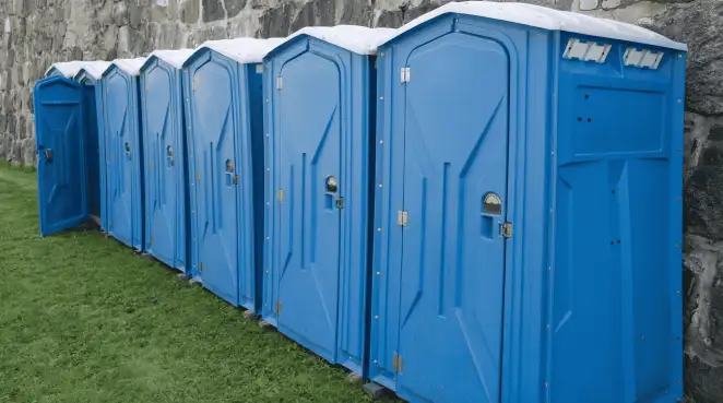 Row of blue portable toilets lined up on grass against a stone wall for event sanitation in Buffalo, NY