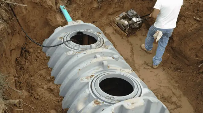 Septic tank installation showing a technician compacting soil around a new poly septic tank in an excavation pit in Buffalo, NY